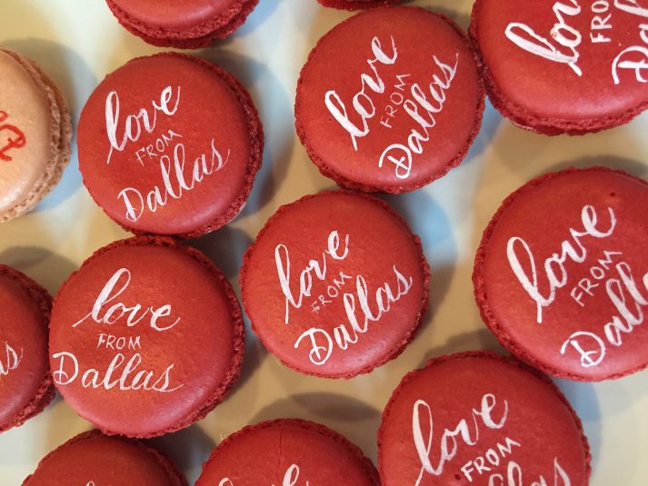 White calligraphy on red macron cookie that says "love from Dallas"