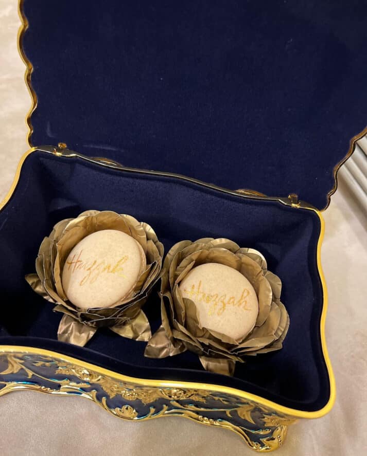 two beige macron cookies sitting in a blue velvet box with golden calligraphy that say "huzzah"